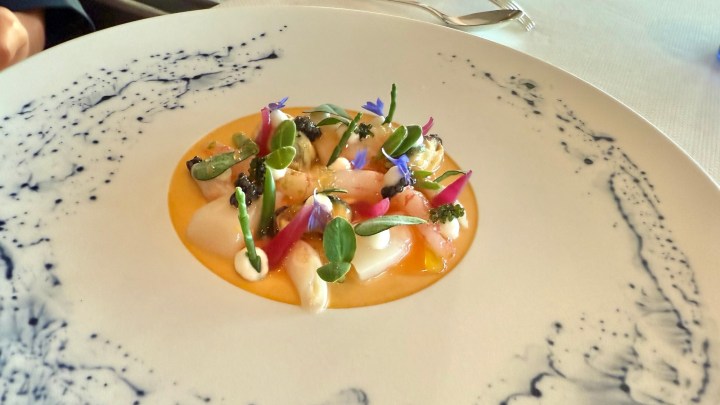 A gourmet seafood dish featuring an array of colorful garnishes, including flowers and vegetables, served on an elegant plate.