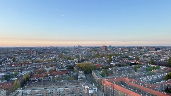 Panoramic view of Amsterdam from the 23rd floor of the Okura hotel at dusk, featuring a mix of urban buildings and green spaces under a clear sky.