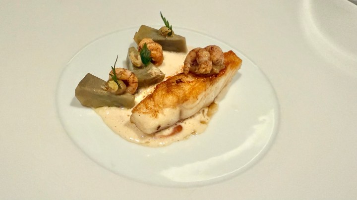 A beautifully plated dish featuring a piece of cooked fish, accompanied by a creamy sauce, shrimp, and green vegetables.