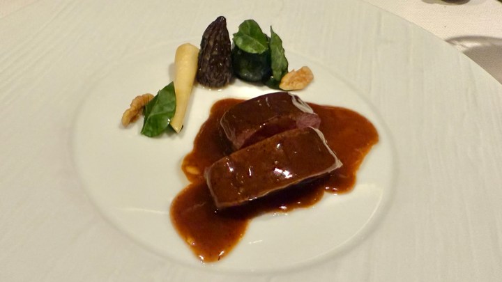 A plated dish featuring breast fillet of poussin de Bresse, accompanied by a rich sauce, morels, small vegetables, and walnuts, arranged artfully on a white plate.