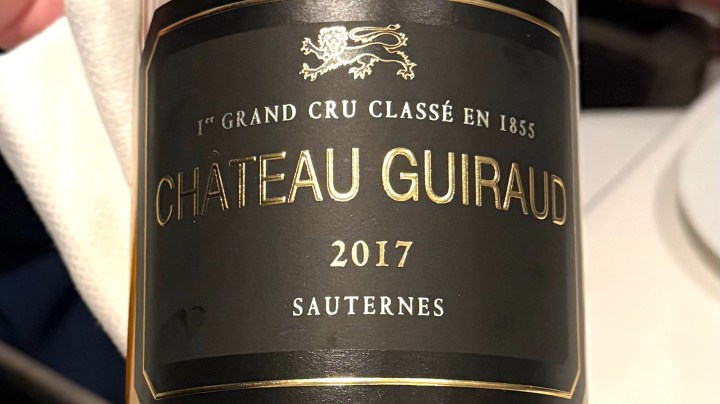 Close-up of a bottle of 2017 Château Guiraud Sauternes wine, showcasing its elegant black label with gold lettering.