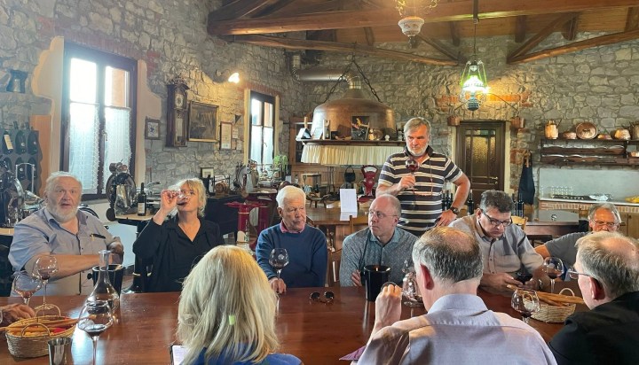 Group of wine connoisseurs gathered around a wooden table in a rustic tasting room, engaged in conversation and tasting wines.