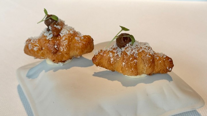 Two croissants stuffed with cheese, topped with a small garnish, served on a white plate.