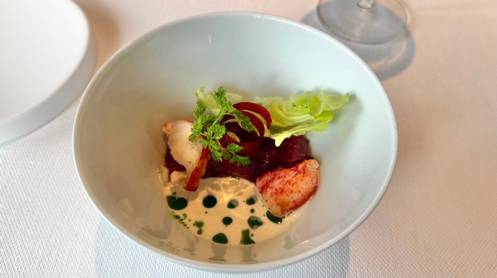 A bowl featuring lobster and raw tuna garnished with green leaves, sauce, and decorative dots of puree.