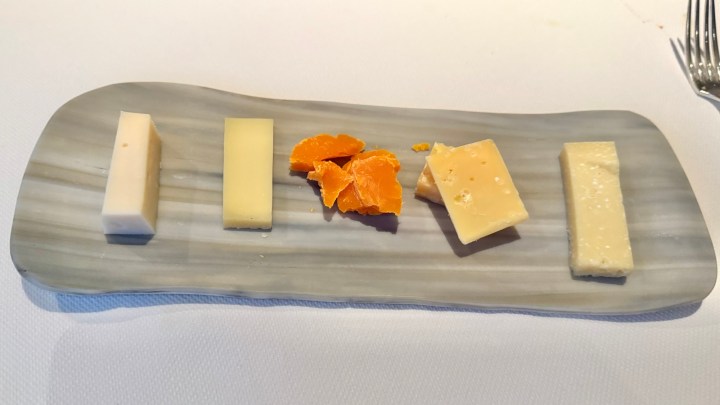 A plate displaying a selection of cheeses, including various cheese blocks and a few orange segments, elegantly arranged on a gray serving dish.