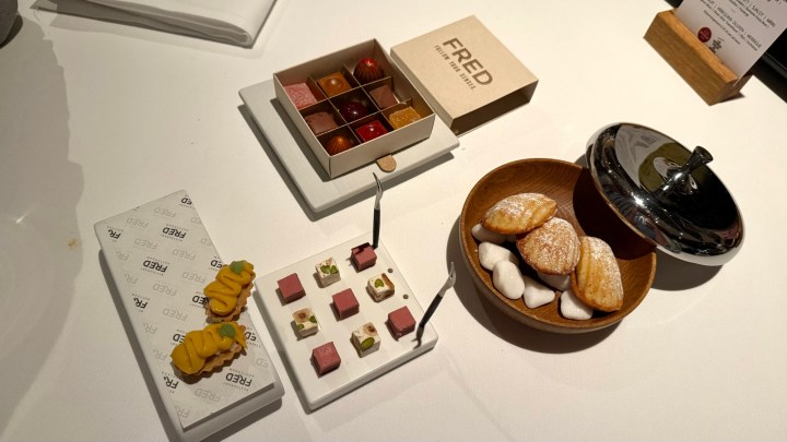An assortment of friandises served at restaurant Fred, including colorful bonbons in a box, a small plate with decorative treats, and madeleines arranged in a bowl.