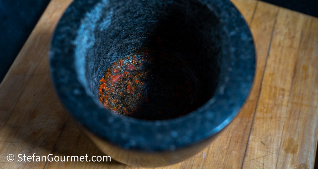 Close-up of a stone mortar with remnants of red chili paste, set on a wooden surface.