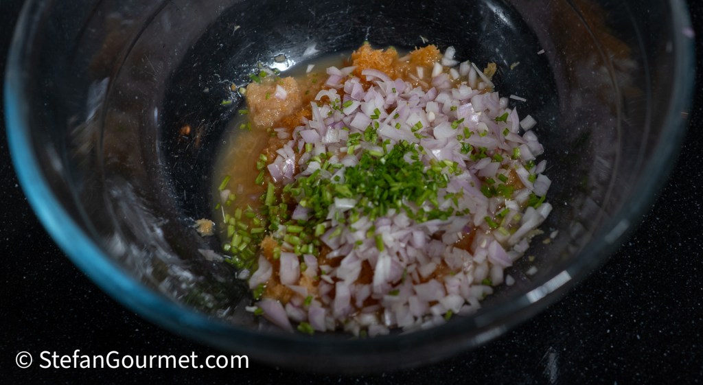 A glass bowl containing minced shallots, dried shrimp, and chopped cilantro stems for a ceviche dressing.