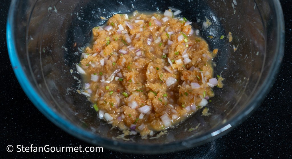 A glass bowl containing a mixture of ground dried shrimp, minced shallots, and chopped herbs, with a slightly chunky texture.