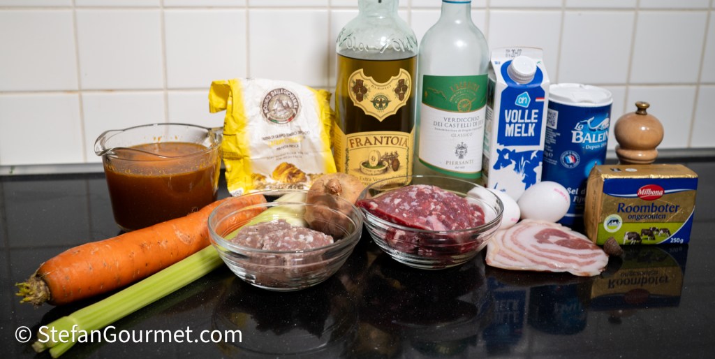 Ingredients for making lasagna, including ground beef, Italian sausage, pancetta, vegetables, eggs, and sauces displayed on a kitchen counter.