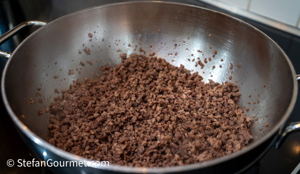 Ground meat in a large stainless steel pan, cooked and crumbled, ready for use in a lasagna.