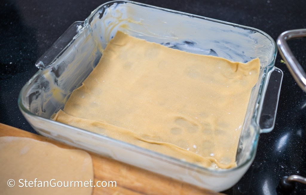 A glass dish lined with fresh pasta sheets ready for lasagna preparation.