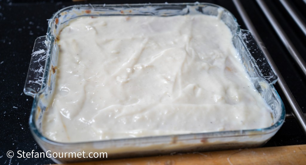 A glass dish filled with a creamy white sauce, likely a _besciamella_, ready to be used in lasagna preparation.