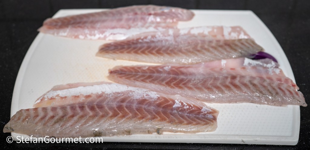 Filleted branzino fish resting on a white cutting board, lightly salted.