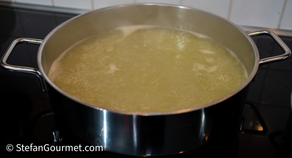 A large pot filled with simmering fish stock, with bubbles forming on the surface.