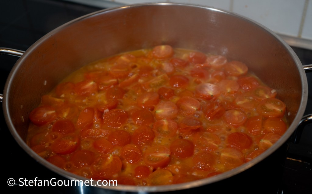 A pot filled with halved cherry tomatoes simmering in a light broth, with steam rising from the mixture.