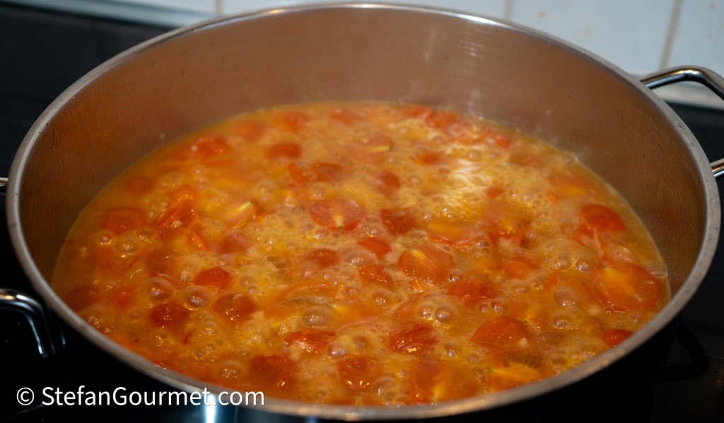 Simmering cherry tomatoes in a pot with bubbling broth.