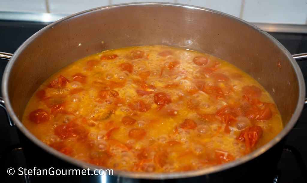 A simmering pot of cherry tomatoes in a flavorful broth, bubbling gently on the stove.