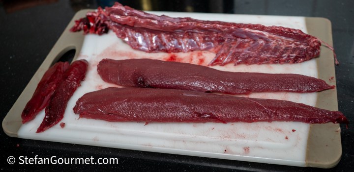 Raw hare fillets and trimmings on a cutting board, showcasing the dark red color of the meat and the gamey texture.