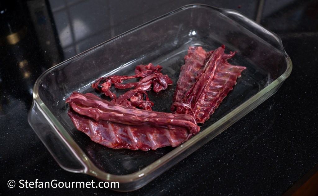 Cuts of raw hare meat arranged in a glass dish on a black countertop.