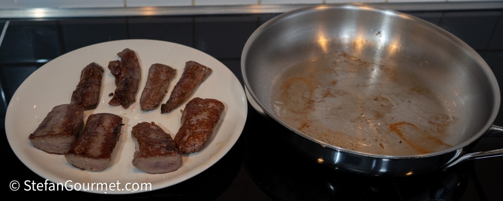 Plate of seared hare fillets beside an empty stainless steel frying pan.
