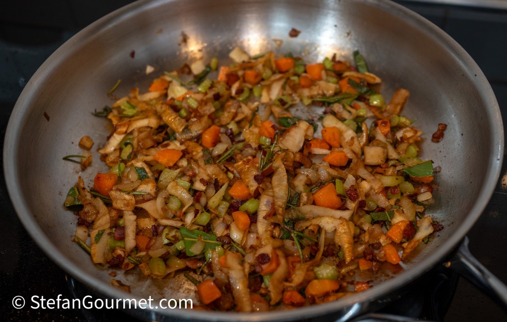 A skillet with sautéed vegetables including chopped celery, carrots, and parsley root, mixed with aromatic herbs like rosemary and sage, creating a colorful medley.