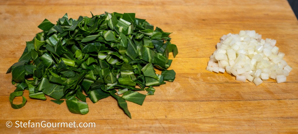 A cutting board with finely chopped chard leaves on the left side and diced onion on the right side.
