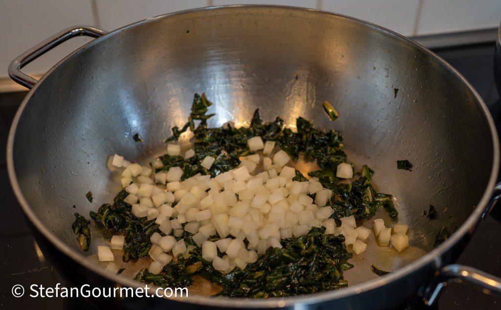 Chopped chard and diced parsley root sautéing in a stainless steel pan, with a few leaves of cooked chard visible.
