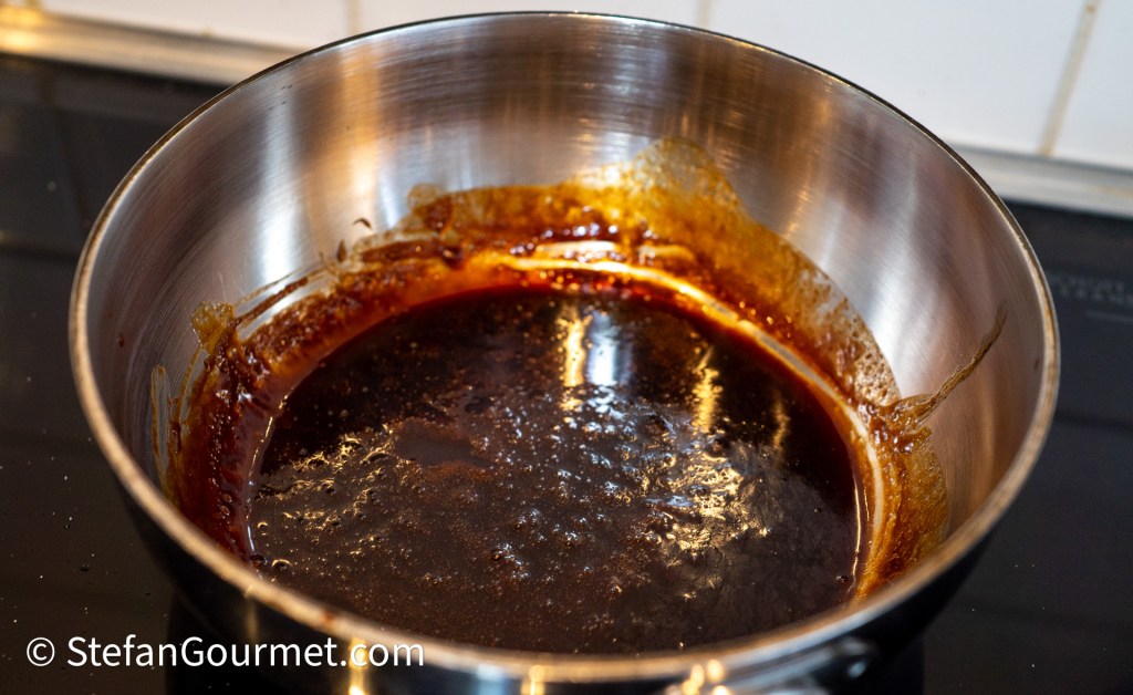 A stainless steel saucepan containing a dark, thick sauce residue, indicating a reduction or caramelization process.