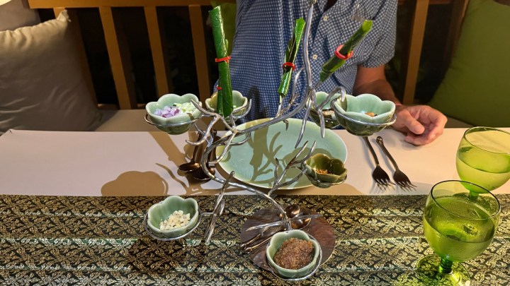 An elegant presentation of traditional Thai appetizers arranged on a decorative tree-like stand, showcasing various condiments and herbs, with a dining table set for two in a cozy atmosphere.