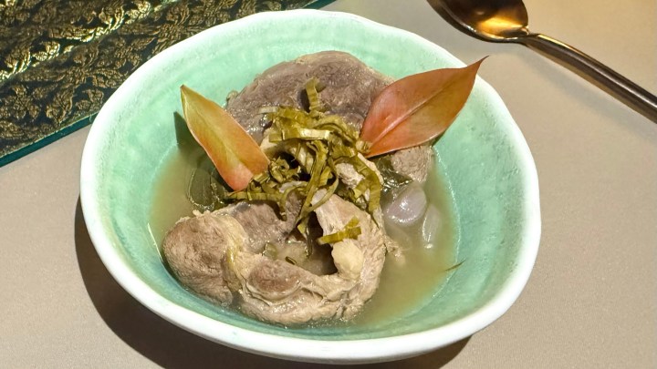 A bowl of beef shank stew in a sour aromatic broth, garnished with leafy greens and herbs, served in a decorative dish.