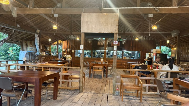 A warm and inviting interior of Ban Suan Lung Khai restaurant, featuring wooden tables and chairs, an open kitchen, and a rustic ceiling in Koh Samui, Thailand.