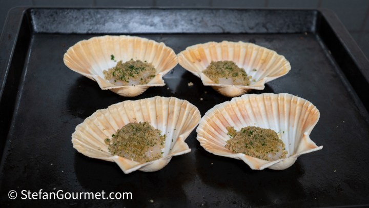 Four scallop shells on a baking tray, each filled with a breadcrumb mixture.