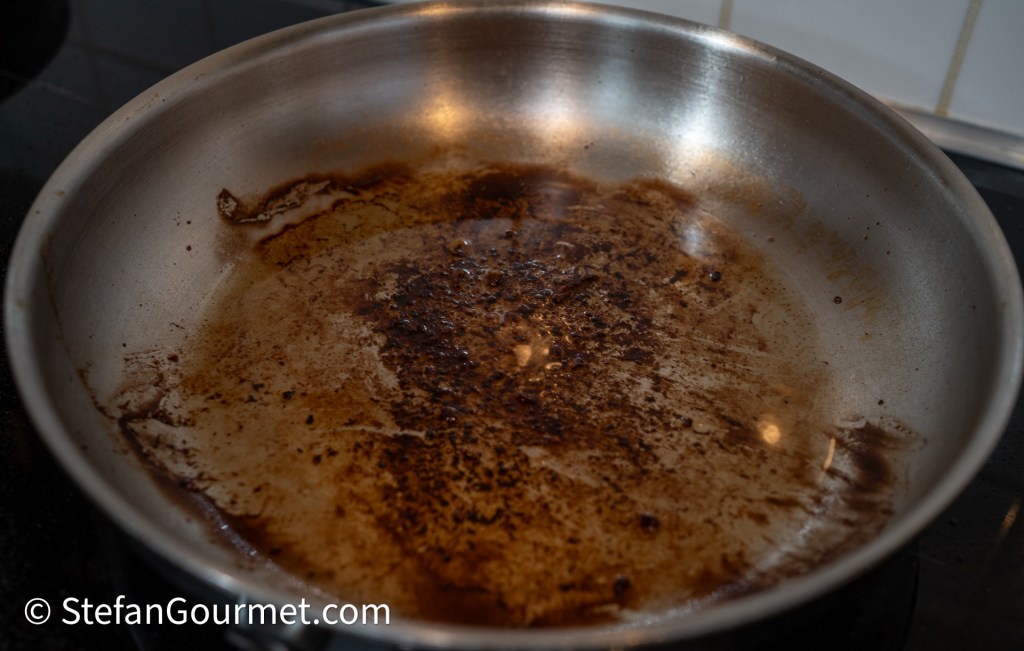 Close-up of a stainless steel frying pan with dark stains and residue, indicating cooking use and a need for cleaning.