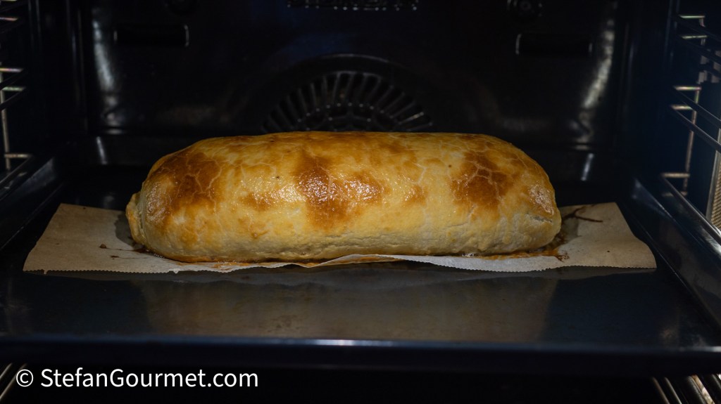 A golden-brown puff pastry loaf baking in an oven on a parchment paper.