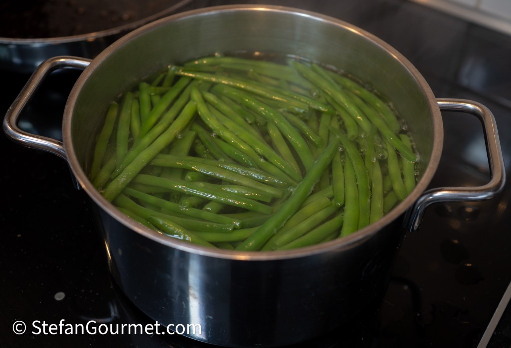 A stainless steel pot filled with boiling water and green beans cooking on a stovetop.