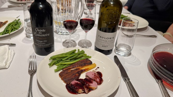 A dinner table setting featuring a plate of sliced duck, green beans, and a sauce, accompanied by two bottles of port wine and glasses of port.