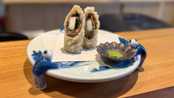 A plate with two pieces of sushi rolls filled with vegetables, served with a small dish of green garnish powder.