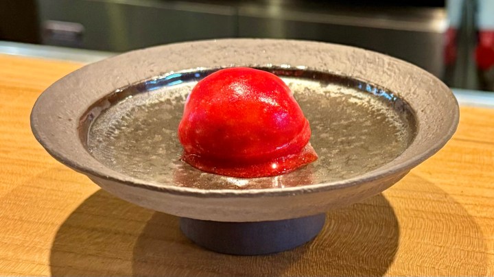A red spherical dessert placed on a textured gray plate, set against a wooden surface.
