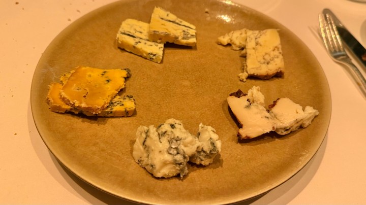 A circular plate displaying six different types of cheese, including blue and yellow varieties, arranged artistically.