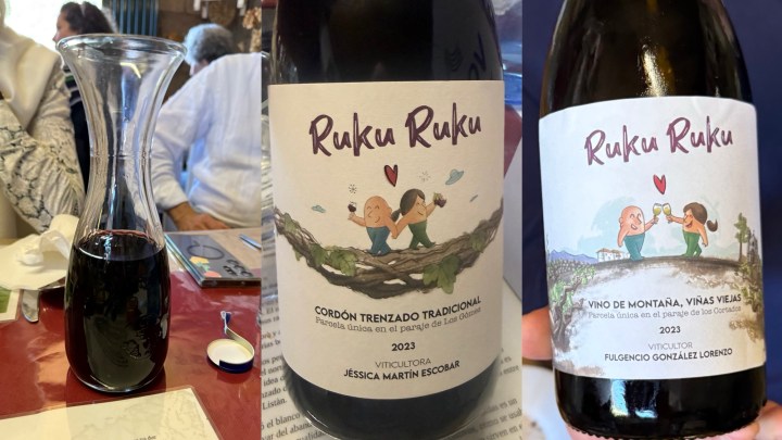 A glass decanter filled with dark red wine on a table, surrounded by people in a restaurant setting.