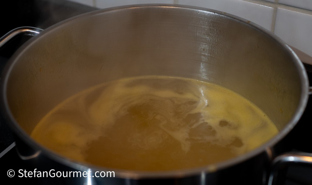 A close-up view of a pot with simmering broth, showing steam rising and a swirling surface.
