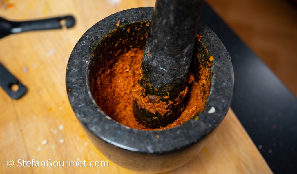 A black stone mortar and pestle with a vibrant orange mixture inside, resting on a wooden surface.