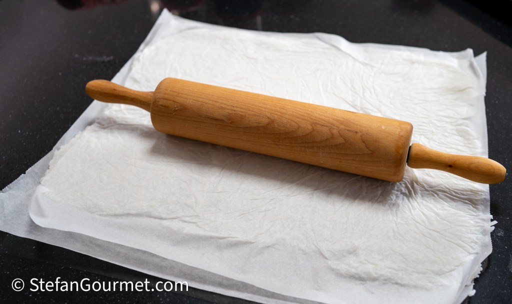 A wooden rolling pin resting on top of a sheet of parchment paper on a dark countertop.