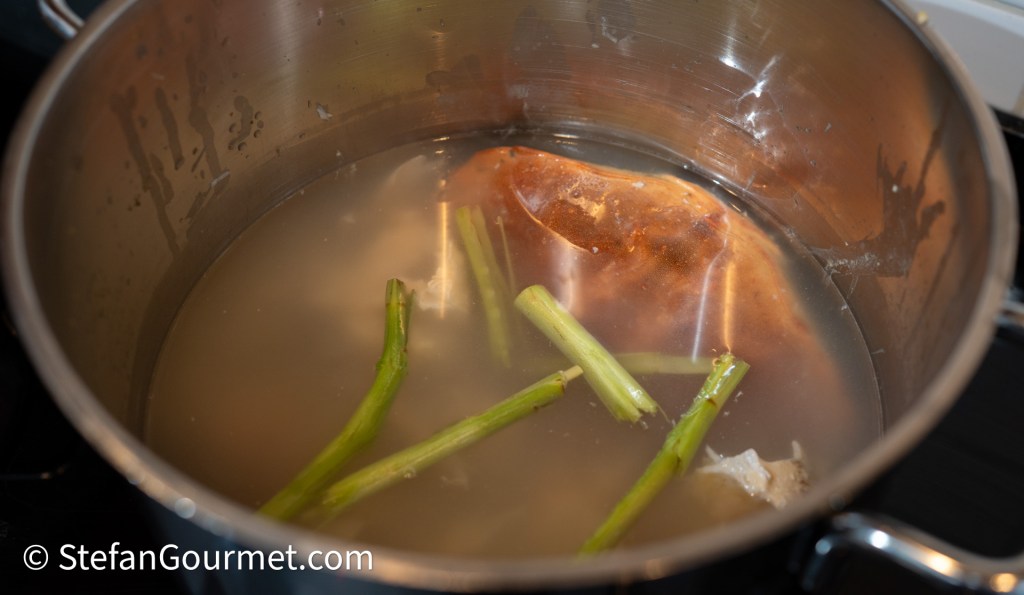 A pot filled with water, containing a piece of meat and green vegetables simmering on a stove.