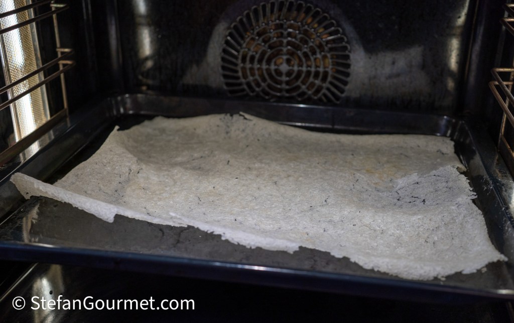A baking tray inside an oven with a thin layer of parchment paper laid flat on it.