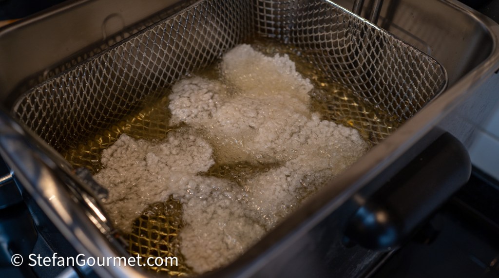 A deep fryer filled with hot oil, with food pieces frying and bubbles forming on the surface.
