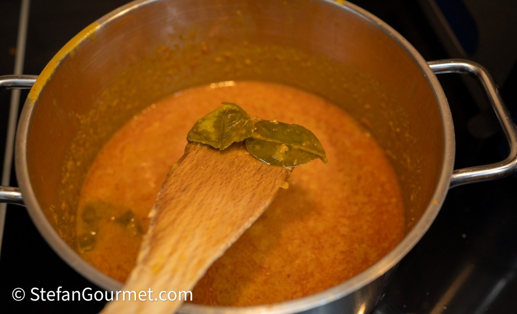 A pot of simmering sauce with a wooden spoon and bay leaves on the surface.