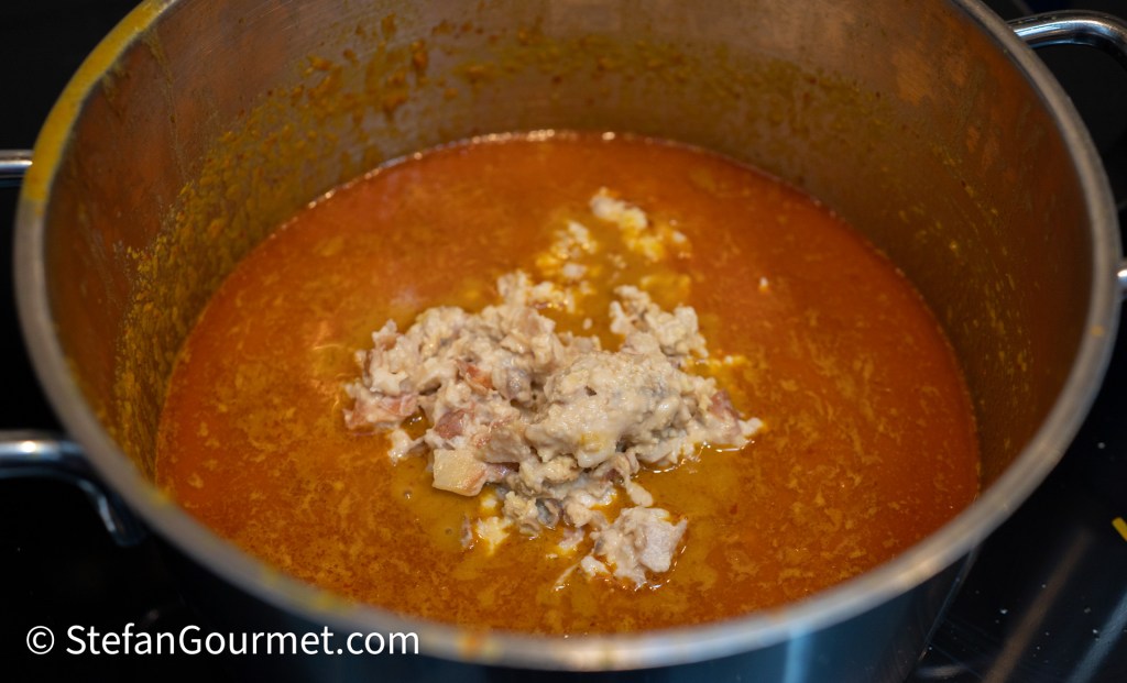 A pot filled with a rich orange sauce and chunks of meat cooking on a stovetop.