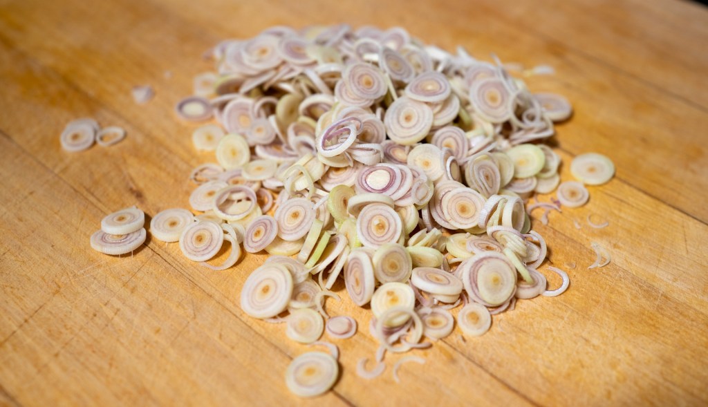 A pile of thinly sliced lemongrass on a wooden cutting board.